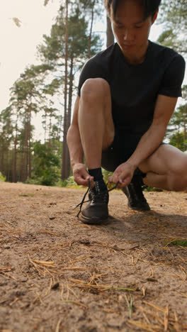 Vídeo-Vertical-De-Primer-Plano-De-Un-Hombre-Atándose-Los-Cordones-De-Una-Zapatilla-Deportiva-Antes-De-Hacer-Ejercicio-Corriendo-Por-Una-Pista-A-Través-De-Un-Bosque,-Filmado-En-Tiempo-Real-2